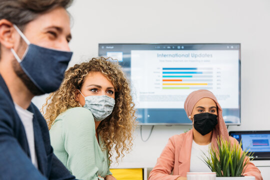Crop multiethnic coworkers in cloth face masks speaking in office
