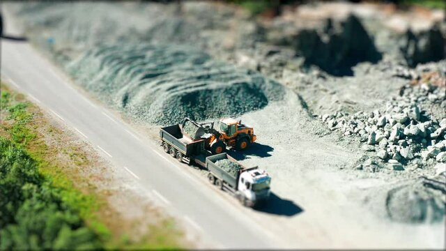 Work at the gravel-making quarry. Bulldozer scooping heaps of gravel and loading it into the waiting trailer. Driver skillfully and efficiantly maneuvers the heavy machinery. A tilt-shift video.