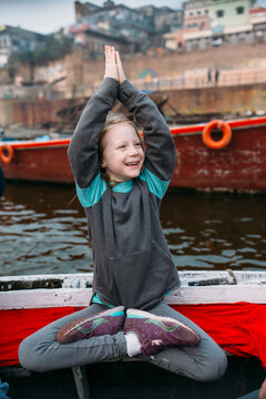 A little girl practicing yoga on a boat in the ganges