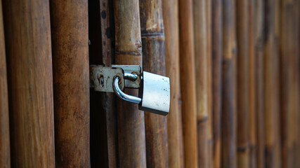 Brown bamboo door or fence, with locked gray padlock. Focus selected