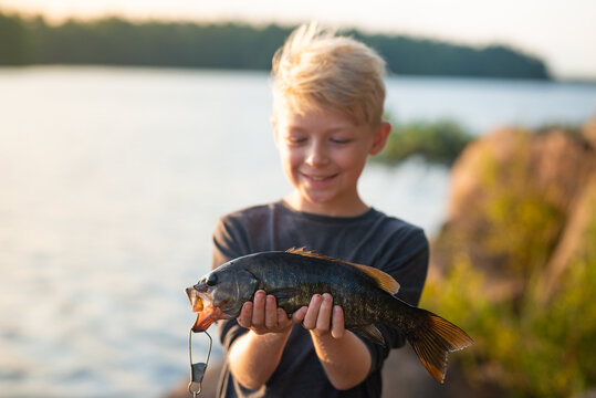 Boy smiling in morning light holds fish on fishing trip vacation