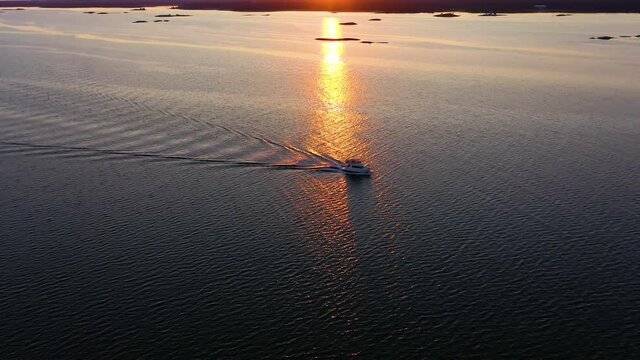 Aerial view of a boat driving in calm, reflecting sea, sunset in Scandinavia - tracking, drone shot