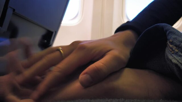 Love couple holding hands on the plane. Boy and girl hands clasped during flight. Unrecognizable man and woman touching hands inside aeroplane.