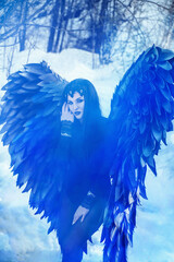 portrait of a beautiful young brunette woman dressed as a black angel in blue smoke