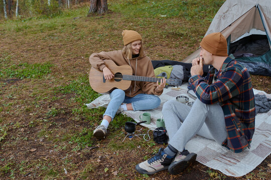 man and woman play guitar camping in forest