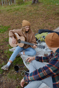 man and woman play guitar camping in forest