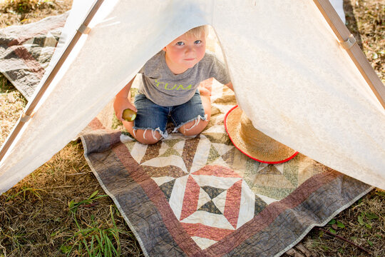 Toddler boy looks up from inside tent
