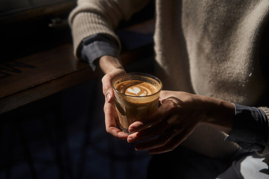 Crop woman resting with cup of latte in dim cafeteria