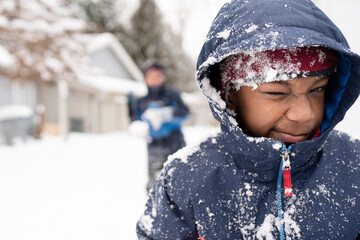 Cute boy covered in snow squints at camera