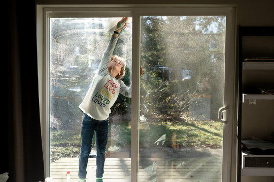 Cute boy stands on porch cleaning sliding glass door