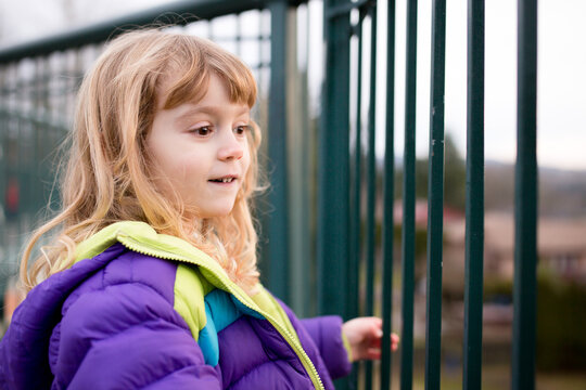 Cute blonde girl in jacket looks through fence rail