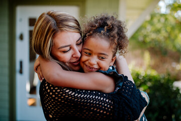 Loving mom embraces smiling biracial daughter on porch of house