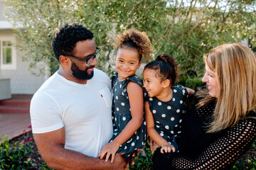 Loving parents holding cute biracial daughters in matching outfits
