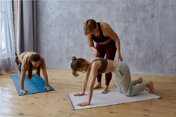 adult mother yoga coach with her daughters doing yoga at home