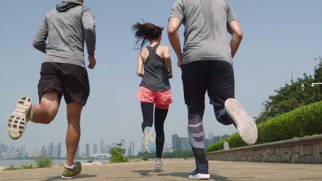 three young asian men and woman running outdoors in a city bay park
