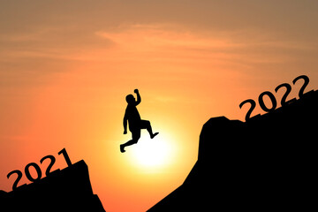 Silhouette of young man jumping between 2021 and 2022 years with beautiful sunset.
