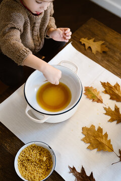 Toddler dipping leaves in melted bees wax