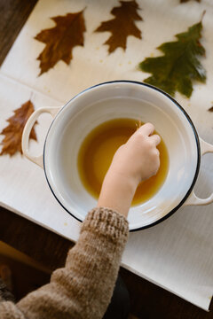 Toddler dipping leaves in melted bees wax
