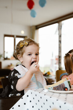 Toddler girl eating cake on a birthday party indoors
