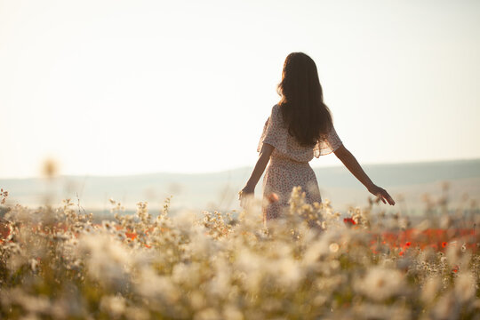 Beautiful girl in summer dress walks in a flower field