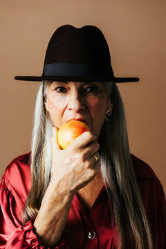 Elegant aged woman in hat eating apple
