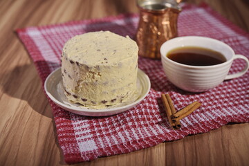 A buttercream cake, a cup of coffee, cinnamon sticks and a turk on the table.