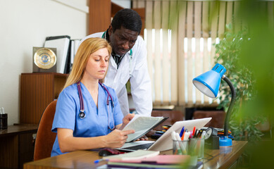 Portrait of two multinational doctors in the office of a resident of the clinic, sitting at a table...