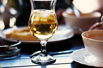 Still life with a large glass of white wine with ice and leftover food in the background