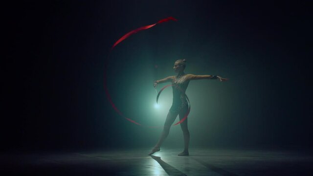 Flexible woman twirling hand with ribbon. Sportswoman dancing in dark space. 
