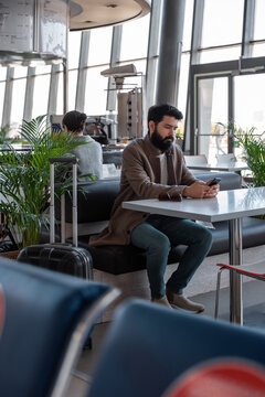 Bearded traveler using smartphone in airport cafe
