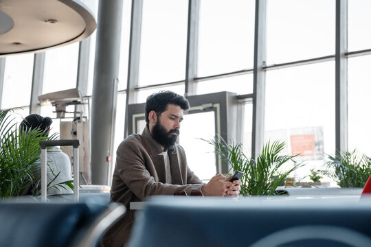 Bearded traveler using smartphone in airport waiting room