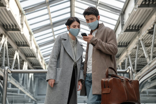 Young couple in masks using mobile phone together in airport