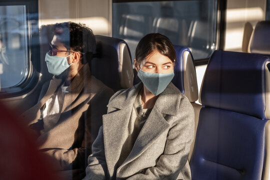 Woman in mask travelling by train with man