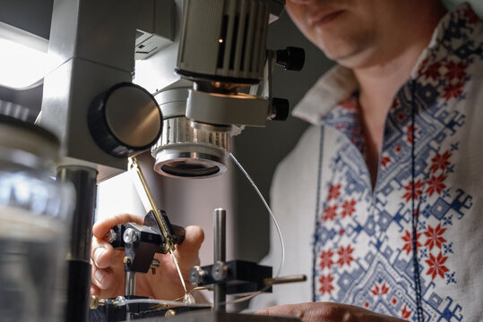 Crop man in Slavic garment inseminating bee under professional microscope