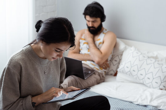 Young woman browsing tablet near boyfriend on bed