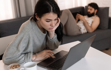 Serious woman using laptop at table near boyfriend