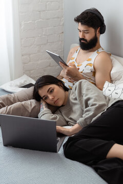 Young couple browsing devices on bed