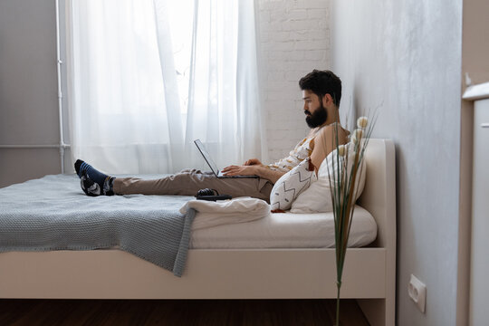 Bearded guy using laptop in bedroom