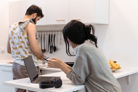 Young woman using smartphone near cooking boyfriend