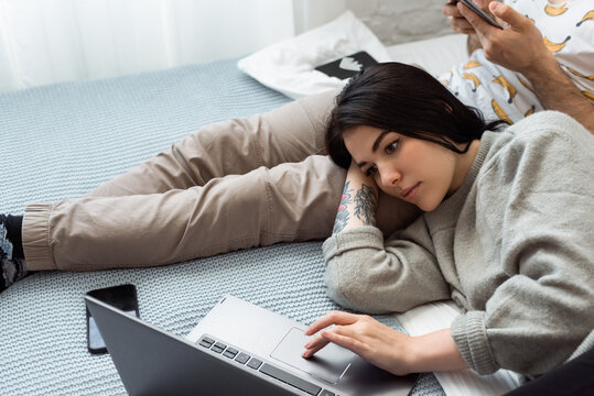 Young woman using laptop on bed near boyfriend