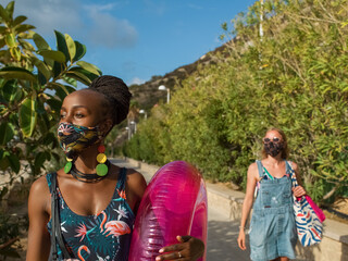 Black woman in mask walking to beach with friend