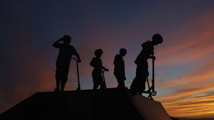Kids with kick scooters against sundown sky
