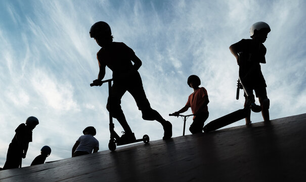 Anonymous boys riding kick scooters on slope against cloudy sky