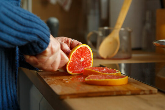 Crop elderly housewife slicing grapefruit at home