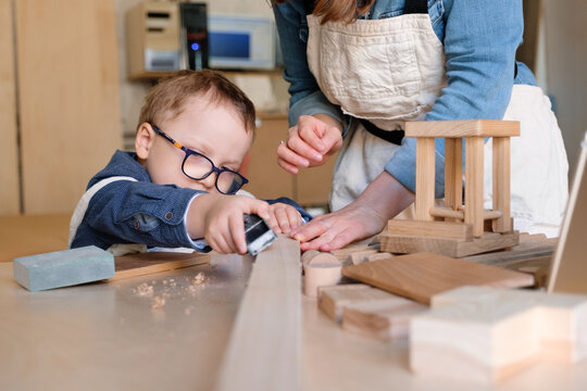 Kid working with joinery tool in carpentry studio with mother