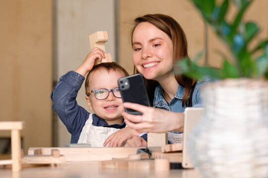 Happy mother and funny kid taking selfie while making wooden toy together