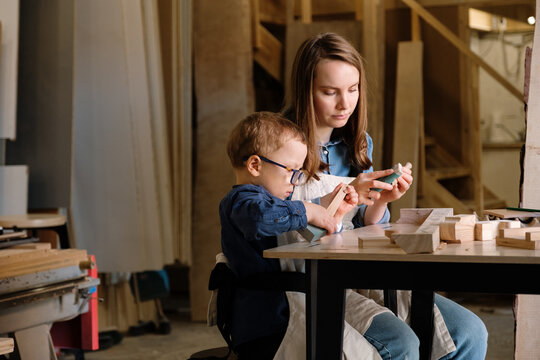 Woman with little kid creating handmade wooden detail in workshop