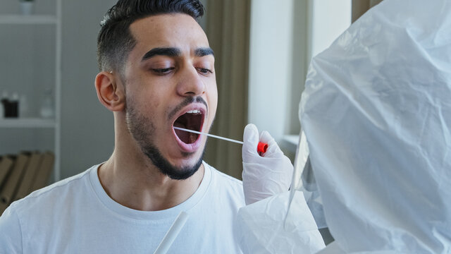 Unrecognizable nurse medical worker doing pcr test with equipment for covid-19 coronavirus to ethnic guy. Close-up spanish man arabic male patient opens mouth donates saliva sample for infection virus