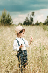Little farmer on a summer field, cute little boy in a straw hat. boy with a flower stands in a field.