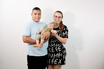 padres latinos sonríen mientras cargan a su bebe mirando a camará